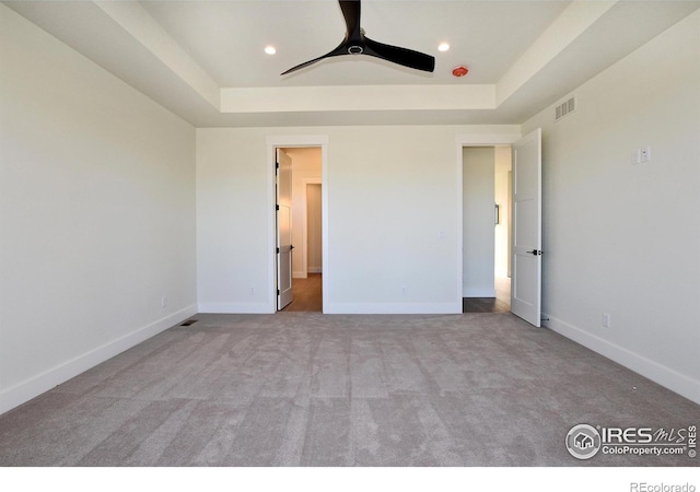 unfurnished bedroom featuring ceiling fan, a raised ceiling, and light carpet