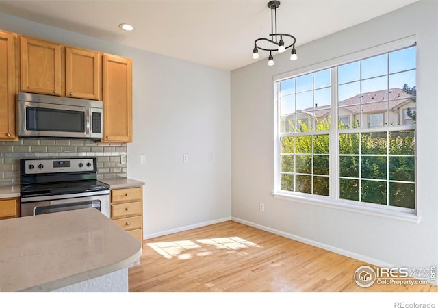 kitchen with appliances with stainless steel finishes, a wealth of natural light, decorative backsplash, and hanging light fixtures