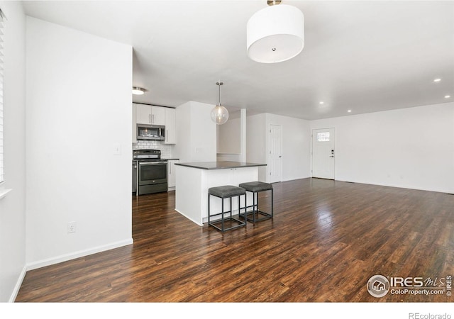 kitchen with appliances with stainless steel finishes, a kitchen bar, hanging light fixtures, white cabinets, and dark hardwood / wood-style floors