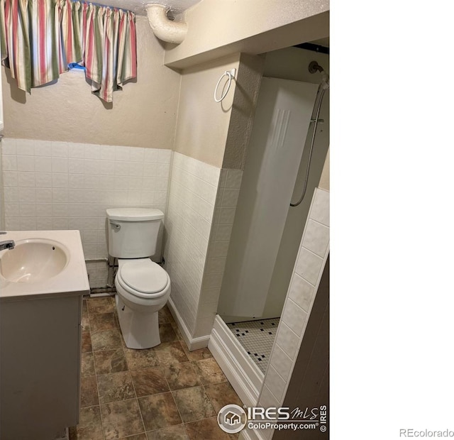 bathroom with tile walls, vanity, toilet, and walk in shower