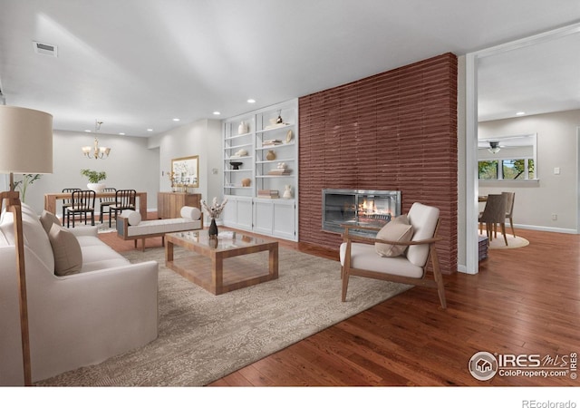 living room featuring a multi sided fireplace, ceiling fan with notable chandelier, hardwood / wood-style floors, and built in features