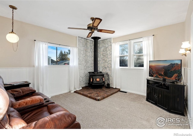 carpeted living room with a wood stove, plenty of natural light, and ceiling fan