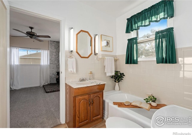 bathroom with toilet, a bathtub, vanity, tile walls, and ceiling fan