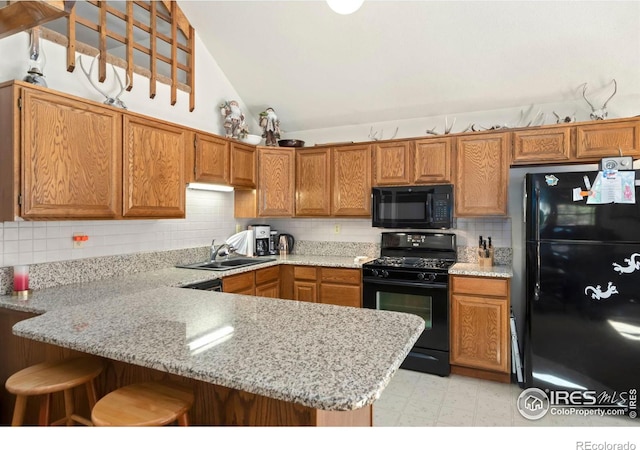 kitchen with black appliances, sink, kitchen peninsula, lofted ceiling, and a breakfast bar