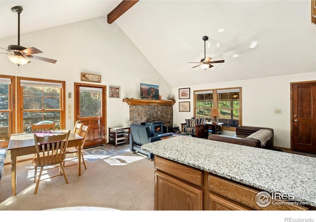 kitchen with a wood stove, ceiling fan, beam ceiling, high vaulted ceiling, and light colored carpet