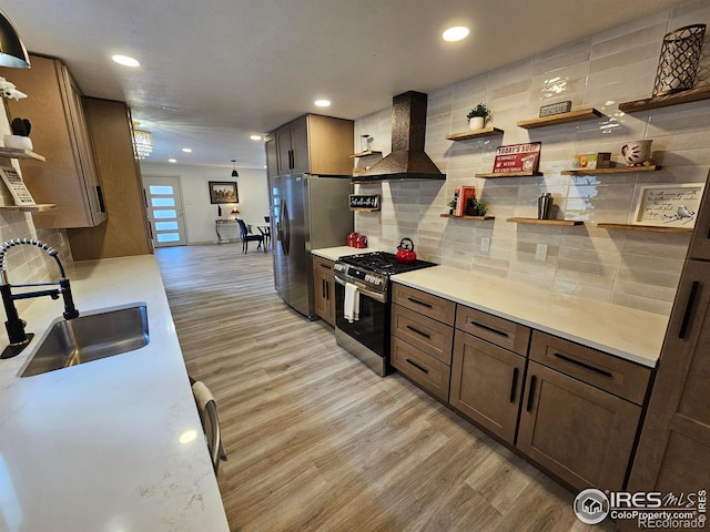 kitchen featuring tasteful backsplash, wall chimney range hood, sink, light wood-type flooring, and stainless steel appliances