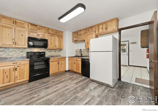 kitchen with sink, decorative backsplash, light stone counters, black appliances, and light hardwood / wood-style flooring