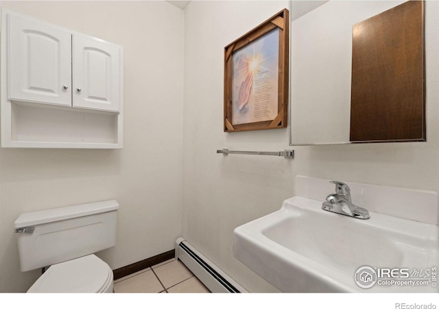 half bathroom featuring toilet, baseboard heating, a sink, baseboards, and tile patterned floors