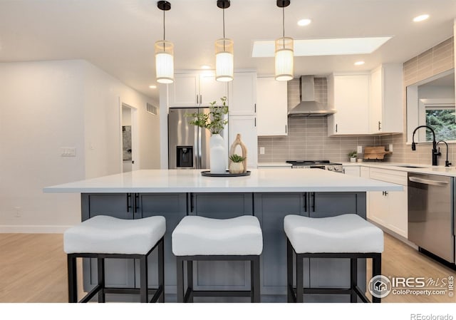 kitchen featuring wall chimney range hood, sink, appliances with stainless steel finishes, a center island, and white cabinets