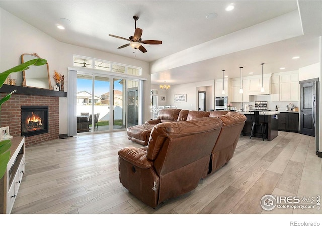 living room featuring a fireplace, ceiling fan with notable chandelier, and light wood-type flooring