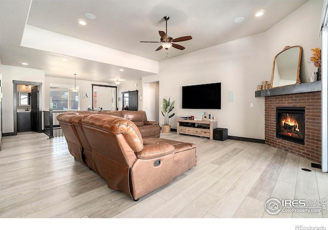 living room with a fireplace, ceiling fan, and light hardwood / wood-style flooring