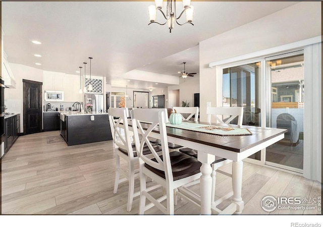 dining room with sink, ceiling fan with notable chandelier, and light hardwood / wood-style flooring