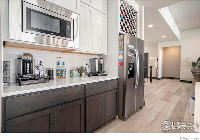 kitchen with white cabinetry, dark brown cabinets, stainless steel appliances, decorative backsplash, and light wood-type flooring