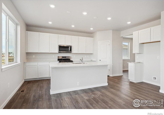 kitchen with dark hardwood / wood-style flooring, white cabinetry, a center island with sink, and appliances with stainless steel finishes