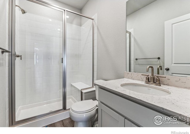 bathroom featuring vanity, a shower with shower door, hardwood / wood-style flooring, and toilet