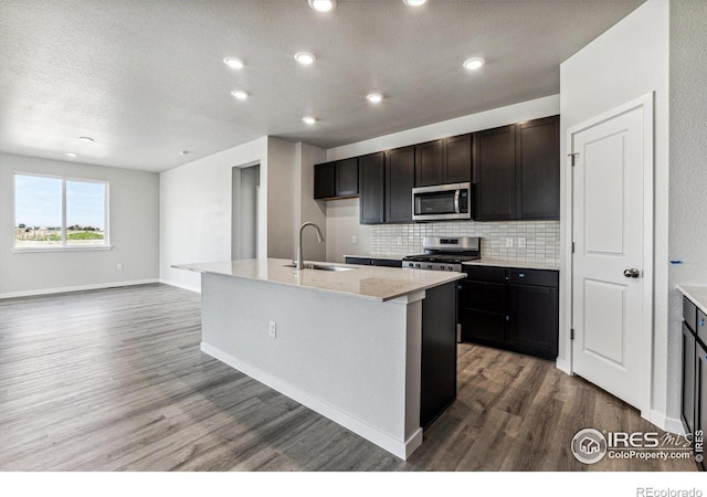 kitchen with a textured ceiling, a kitchen island with sink, wood-type flooring, sink, and stainless steel appliances