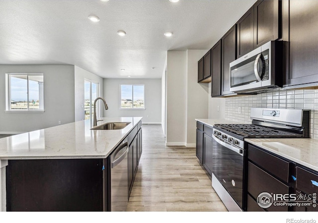 kitchen with light hardwood / wood-style flooring, stainless steel appliances, sink, and an island with sink