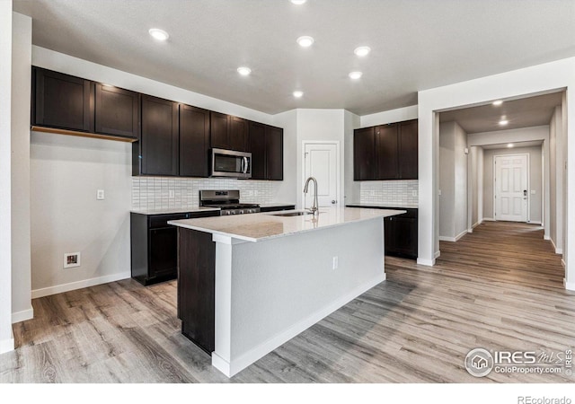 kitchen with sink, appliances with stainless steel finishes, light hardwood / wood-style flooring, and an island with sink