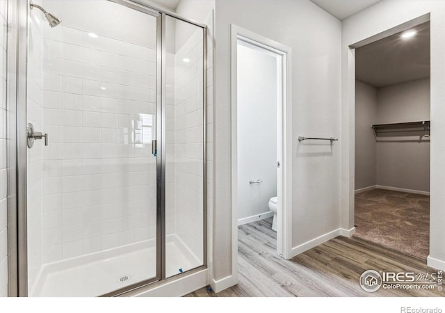 bathroom featuring toilet, a shower with shower door, and wood-type flooring