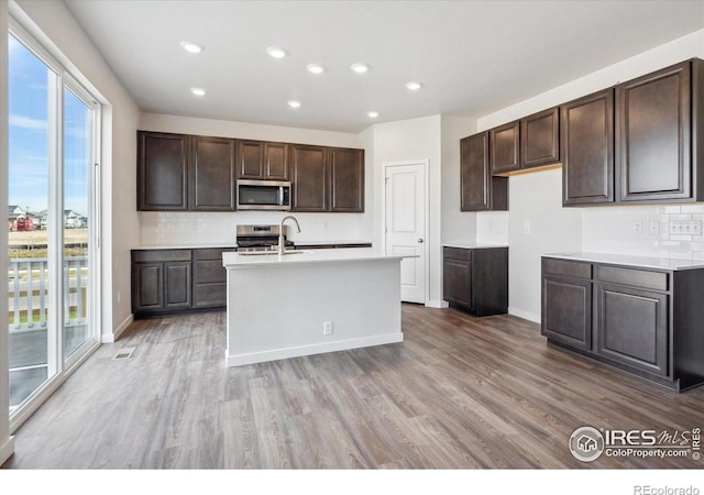 kitchen with light wood-type flooring, an island with sink, appliances with stainless steel finishes, and tasteful backsplash