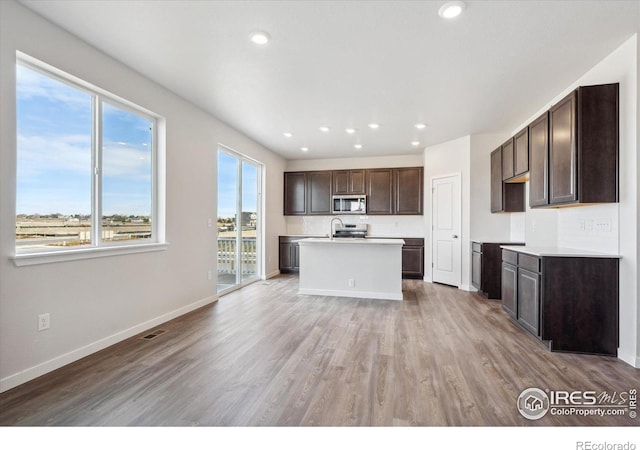 kitchen featuring tasteful backsplash, dark brown cabinets, stainless steel appliances, hardwood / wood-style flooring, and an island with sink