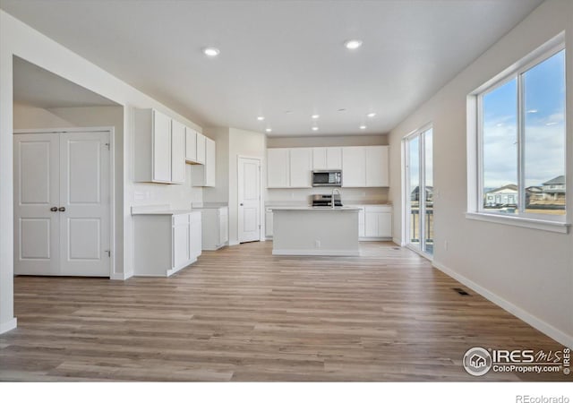 kitchen featuring white cabinetry, a kitchen island with sink, light hardwood / wood-style flooring, and appliances with stainless steel finishes