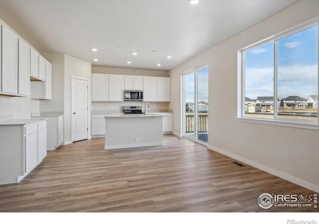 kitchen featuring light wood-type flooring, white cabinetry, stainless steel appliances, and an island with sink