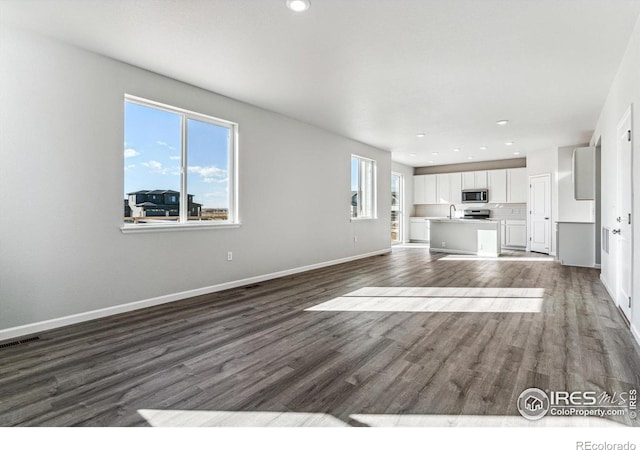 unfurnished living room featuring visible vents, baseboards, dark wood-type flooring, recessed lighting, and a sink
