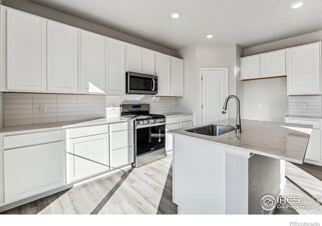 kitchen with white cabinets, appliances with stainless steel finishes, a kitchen island with sink, light wood-type flooring, and sink