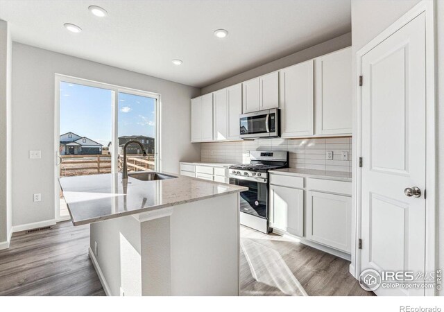kitchen with a sink, light wood-style flooring, appliances with stainless steel finishes, and tasteful backsplash