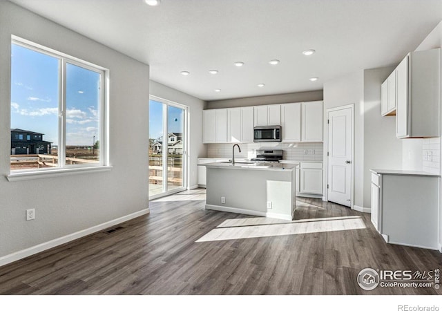 kitchen with decorative backsplash, a center island with sink, white cabinetry, dark hardwood / wood-style floors, and stainless steel appliances