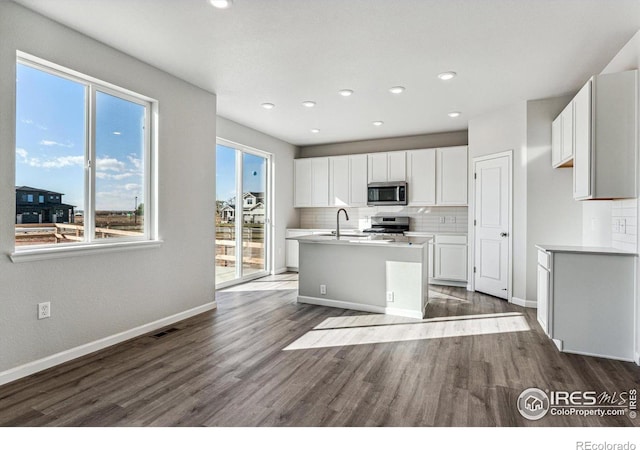 kitchen with an island with sink, white cabinets, appliances with stainless steel finishes, tasteful backsplash, and dark wood-style floors