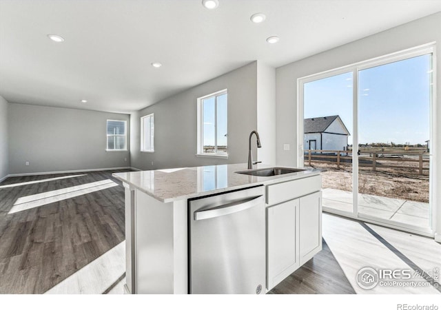 kitchen featuring light stone countertops, a sink, dishwasher, light wood-style flooring, and open floor plan