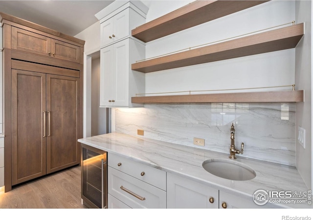 kitchen featuring sink, light hardwood / wood-style flooring, light stone countertops, white cabinetry, and beverage cooler