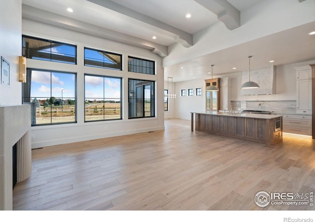 kitchen with white cabinets, light hardwood / wood-style floors, a spacious island, and beam ceiling