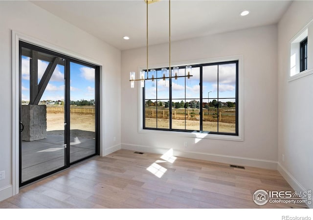 unfurnished dining area with a chandelier, light hardwood / wood-style floors, and a wealth of natural light