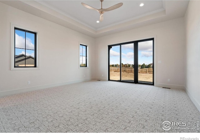 carpeted empty room featuring ceiling fan, a healthy amount of sunlight, and a tray ceiling