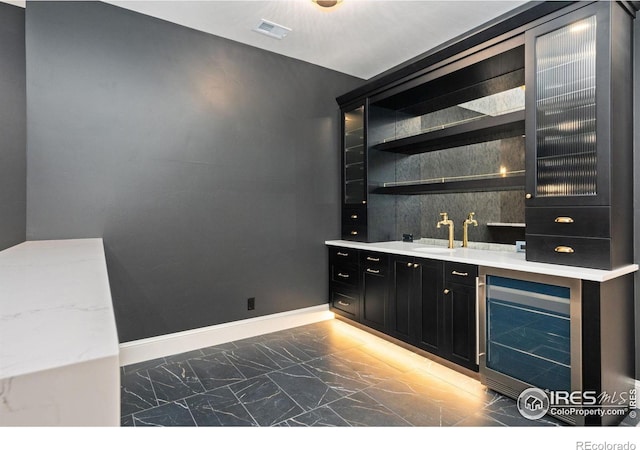 bar with wine cooler, light stone counters, and sink