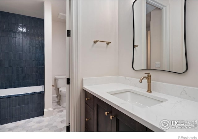 bathroom with tiled bath, vanity, and toilet