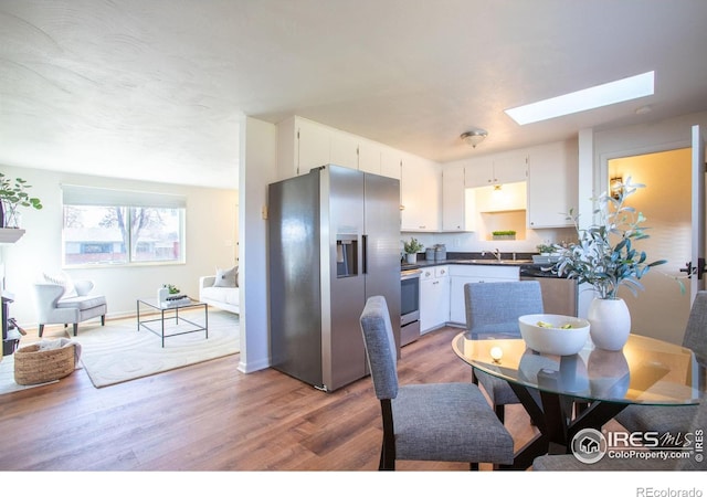 kitchen featuring white cabinets, sink, a skylight, hardwood / wood-style flooring, and appliances with stainless steel finishes