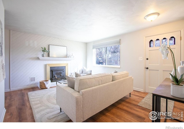 living room featuring wood walls, dark wood-type flooring, and a tiled fireplace