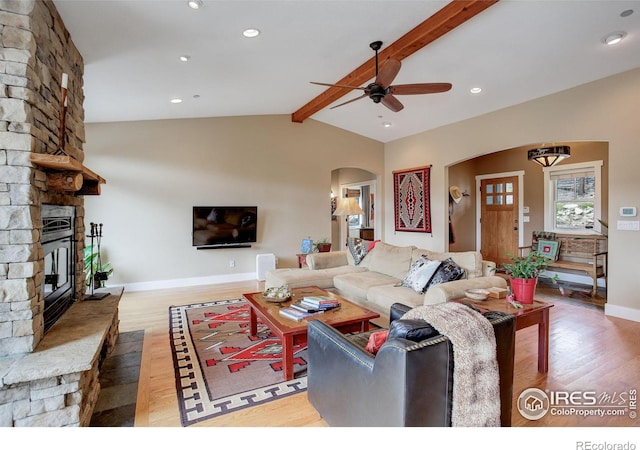 living room featuring ceiling fan, hardwood / wood-style flooring, lofted ceiling with beams, and a stone fireplace