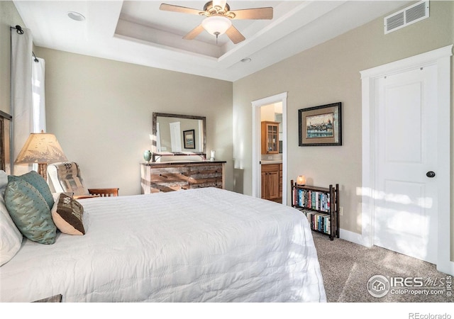 bedroom with carpet floors, a tray ceiling, connected bathroom, and ceiling fan