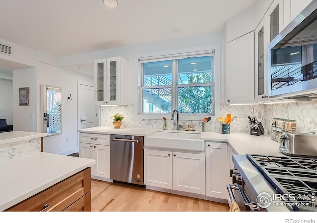 kitchen with decorative backsplash, light wood-type flooring, stainless steel appliances, sink, and white cabinetry