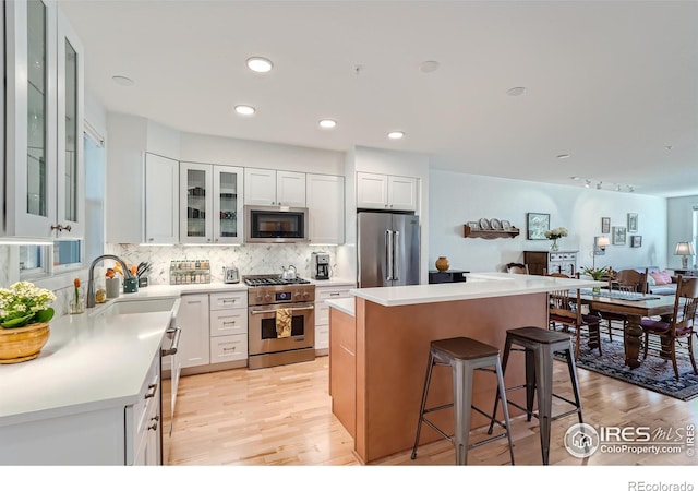 kitchen featuring a center island, high end appliances, light wood-type flooring, white cabinetry, and a breakfast bar area