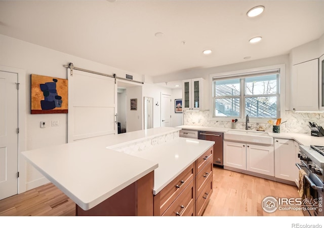 kitchen with stainless steel appliances, sink, a barn door, light hardwood / wood-style flooring, and white cabinets