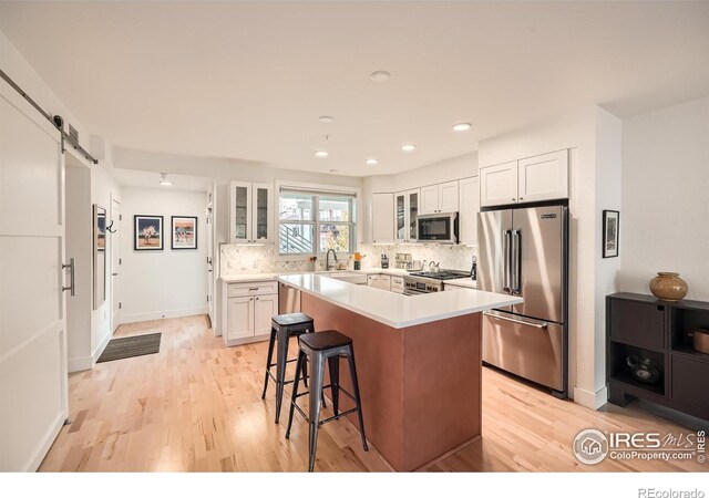 kitchen with stainless steel appliances, a barn door, light hardwood / wood-style flooring, white cabinets, and a center island