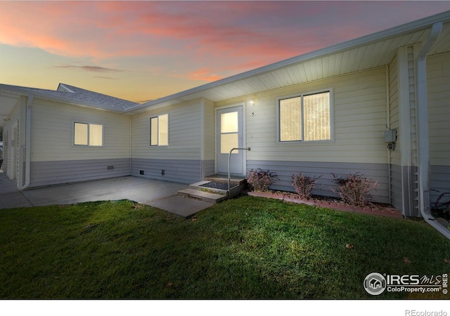 back house at dusk with a patio and a yard