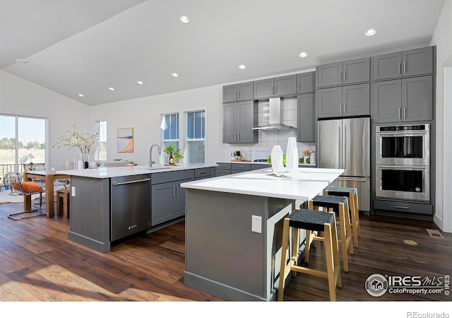 kitchen with a breakfast bar, appliances with stainless steel finishes, a center island, and wall chimney range hood