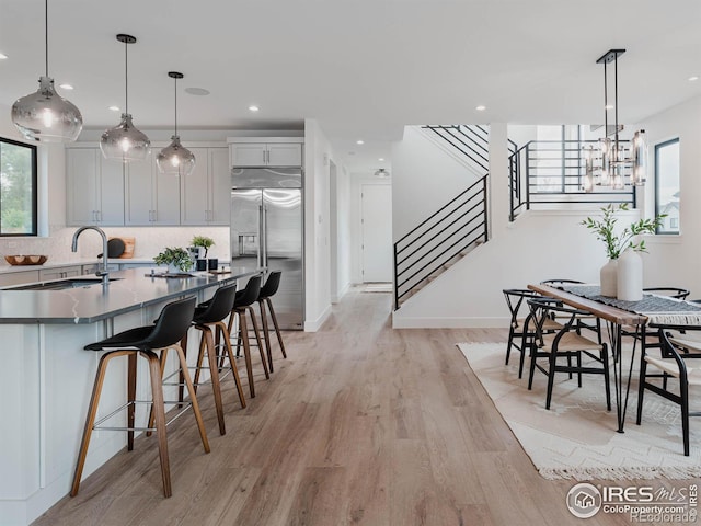 kitchen featuring high end refrigerator, hanging light fixtures, a kitchen bar, light hardwood / wood-style floors, and tasteful backsplash